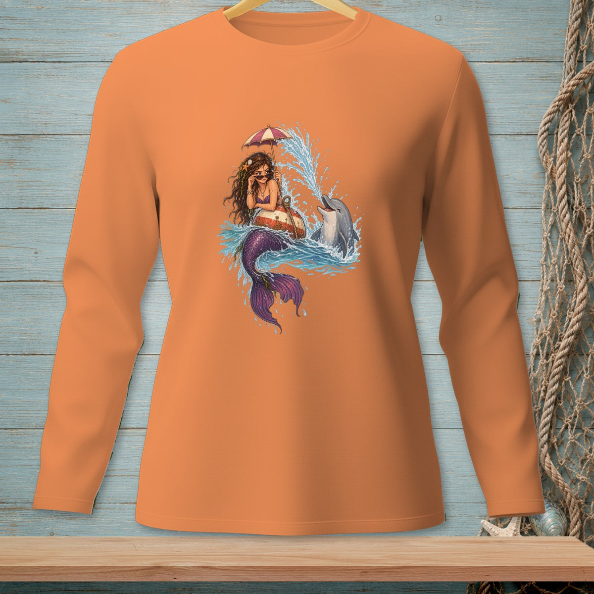 Long sleeve orange t-shirt with a graphic of a mermaid holding an umbrella and a dolphin splashing.