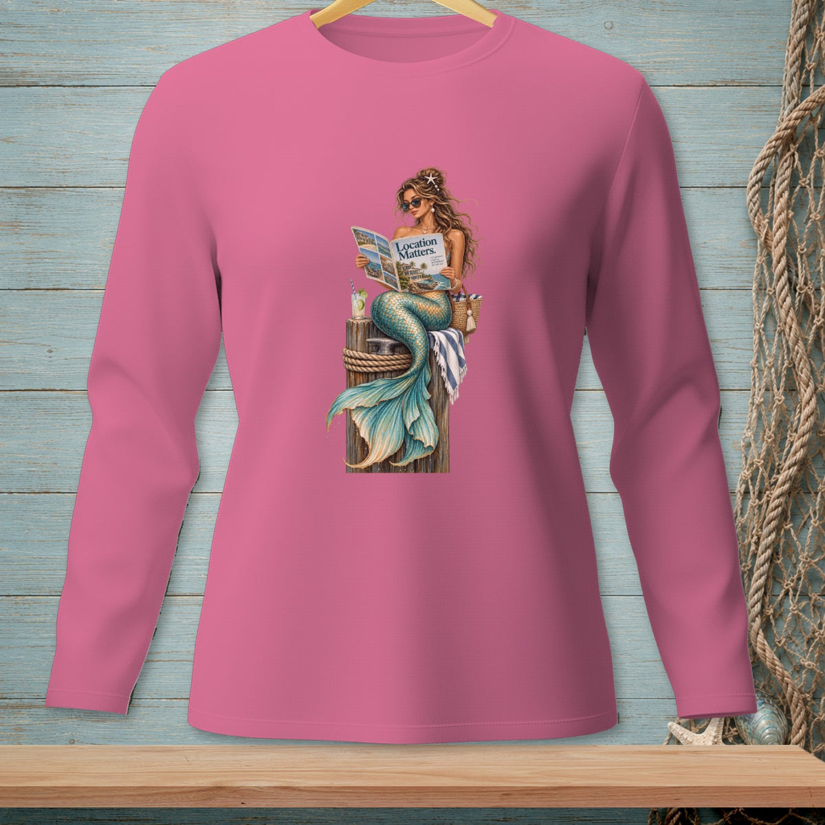 Mermaid with starfish hair reads "Location Matters" magazine while sitting on a dock.