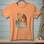 Peach t-shirt featuring two mermaids sitting on a dock, one holding a mirror.