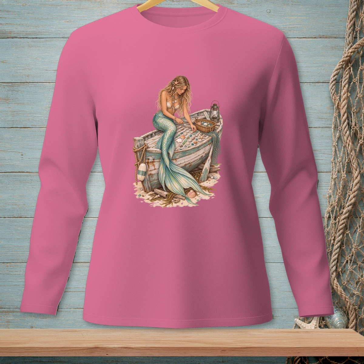 Pink long sleeve shirt with a mermaid sitting on an old boat filled with shells.