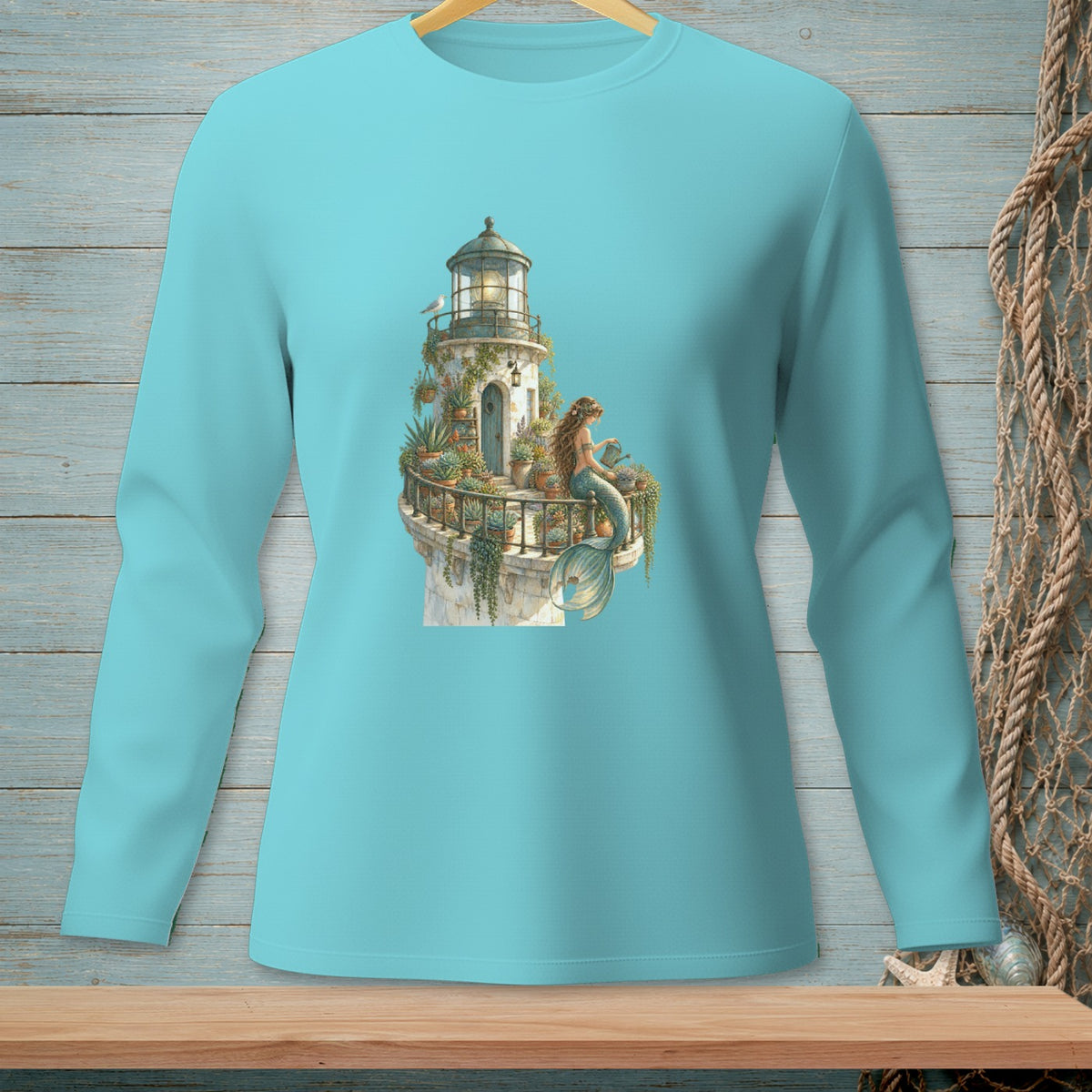 Teal long-sleeve shirt with a graphic of a lighthouse and a mermaid tending plants.