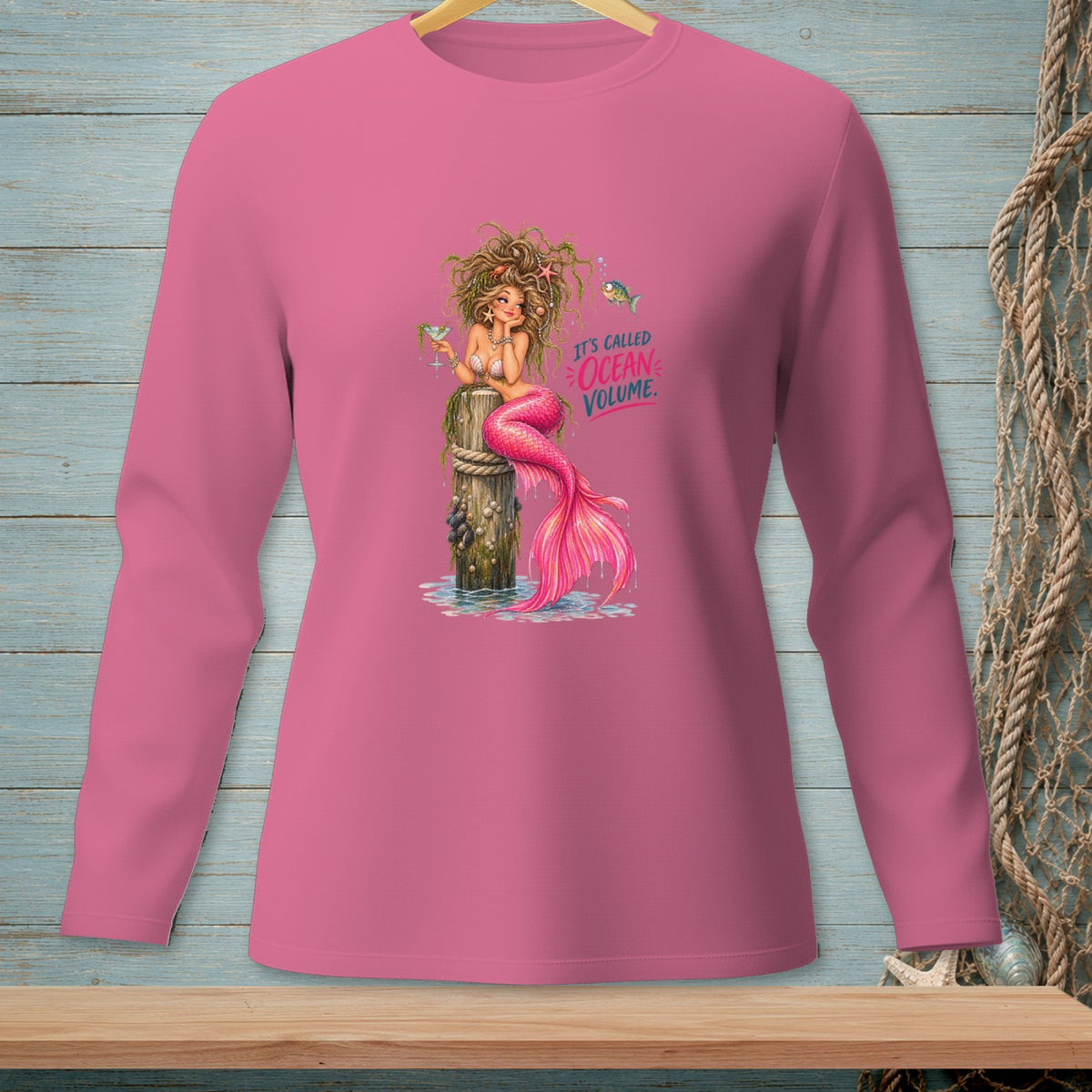 Pink long-sleeve shirt with a mermaid sitting on a post and text reading "IT'S CALLED OCEAN VOLUME."