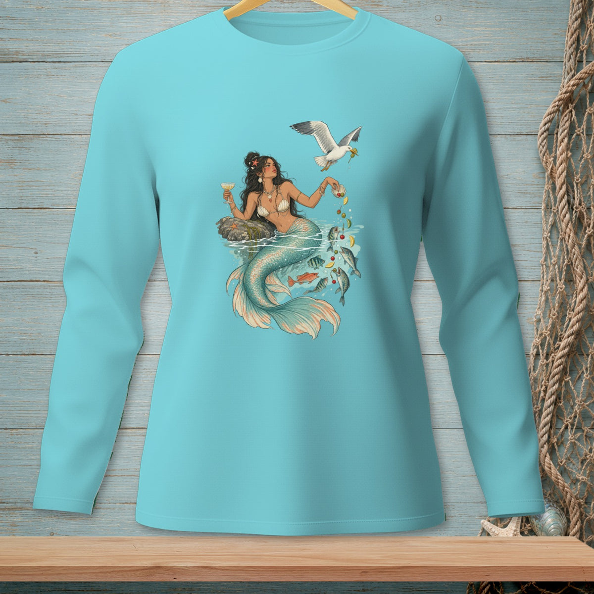 Turquoise long-sleeve shirt featuring a mermaid, fish, and seagull with food.