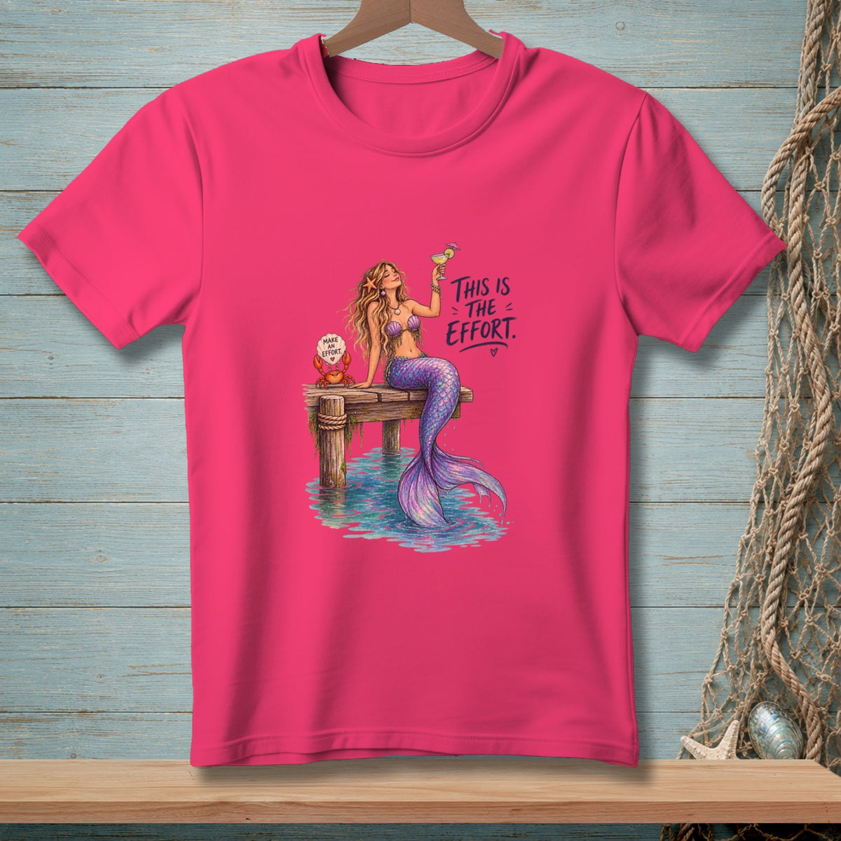 Pink t-shirt with mermaid on dock, holding a drink, and text "This is the effort."
