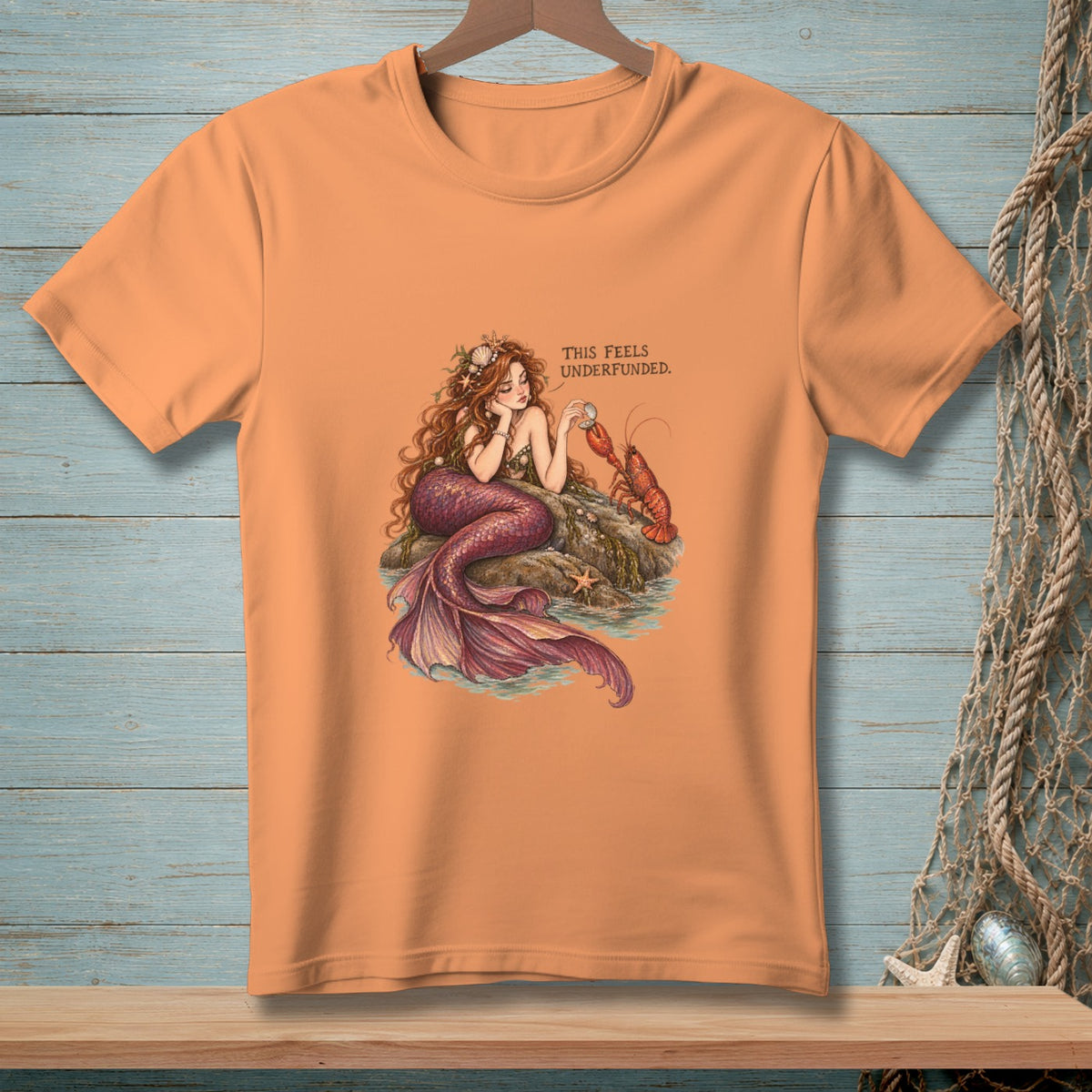 T-shirt with mermaid and lobster illustration and text "THIS FEELS UNDERFUNDED."