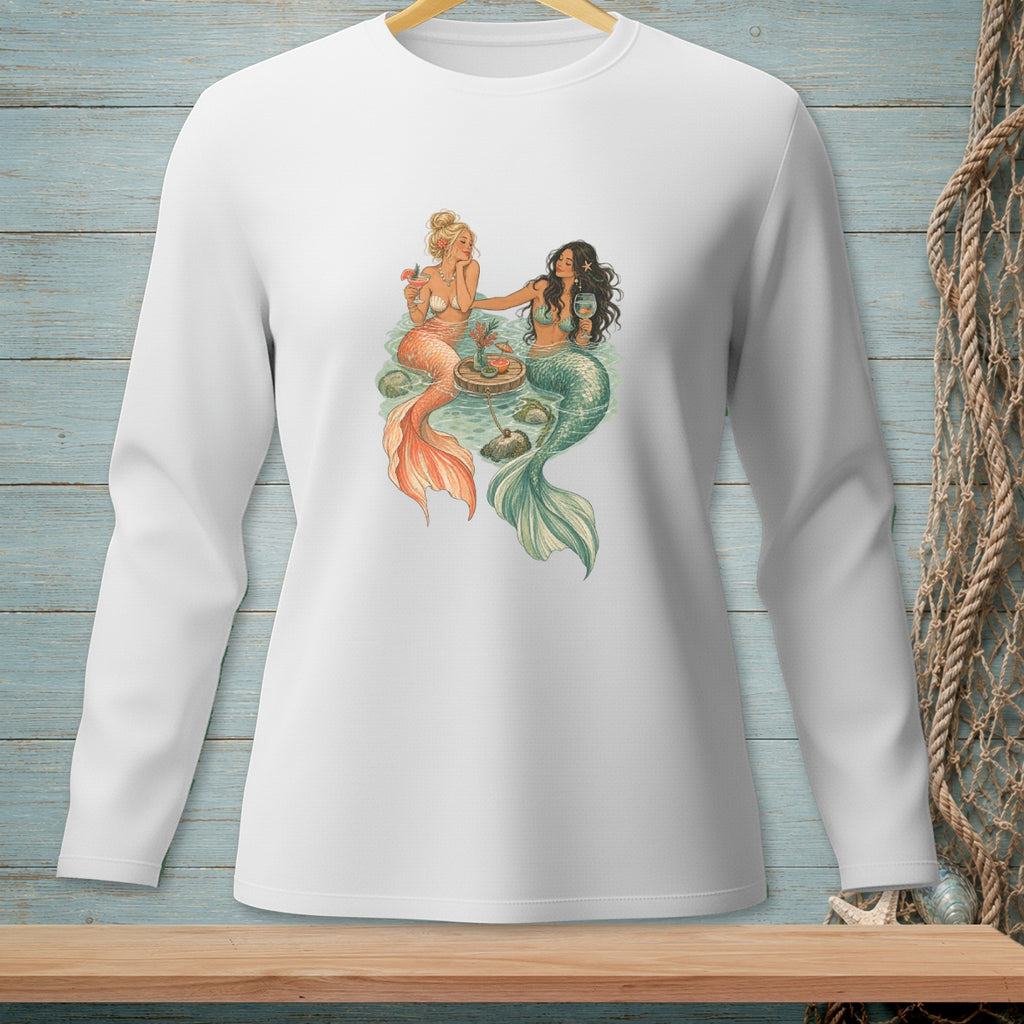 Two mermaids with tails, one orange and one green, sit by a floating table with drinks.