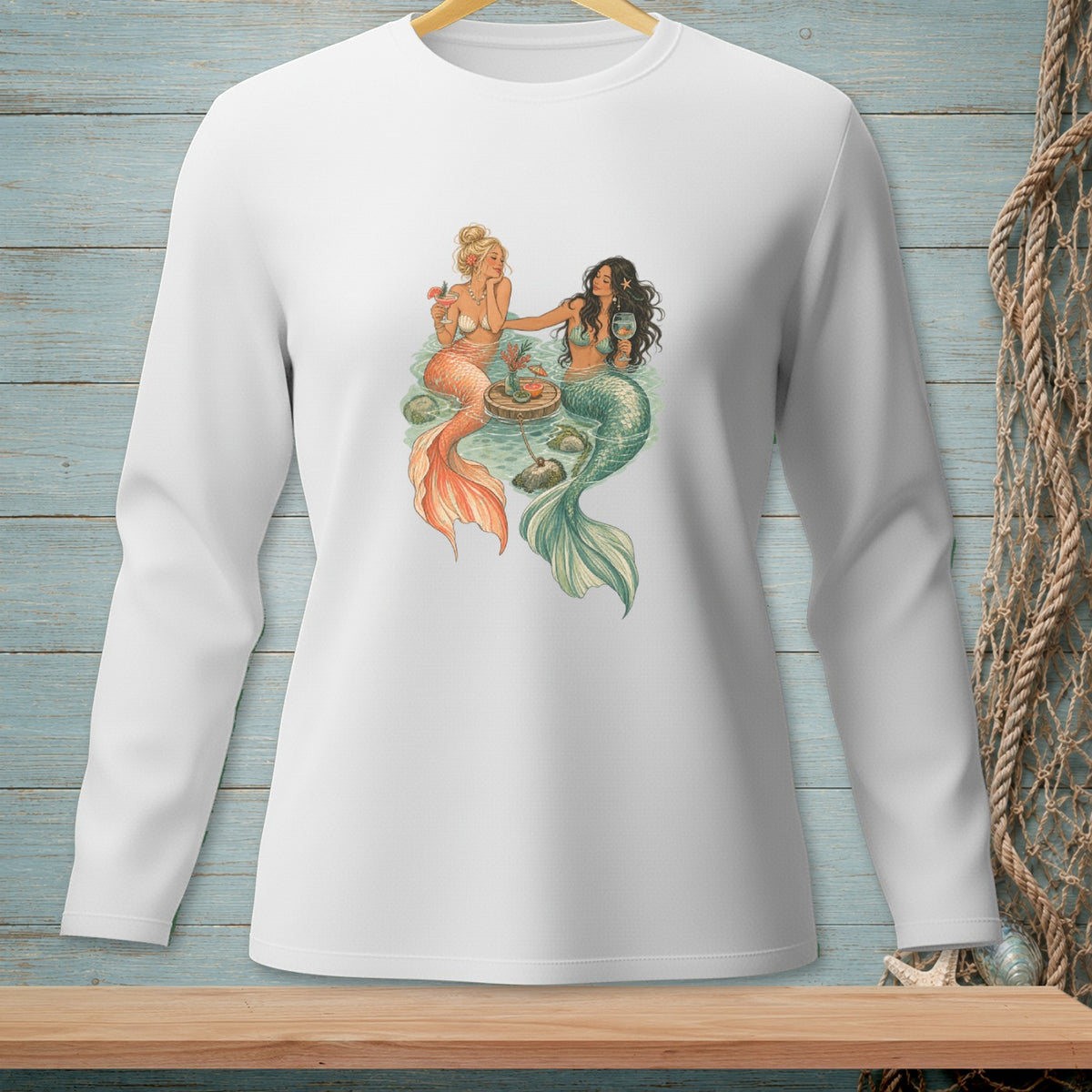 Two mermaids with tails, one orange and one green, sit by a floating table with drinks.