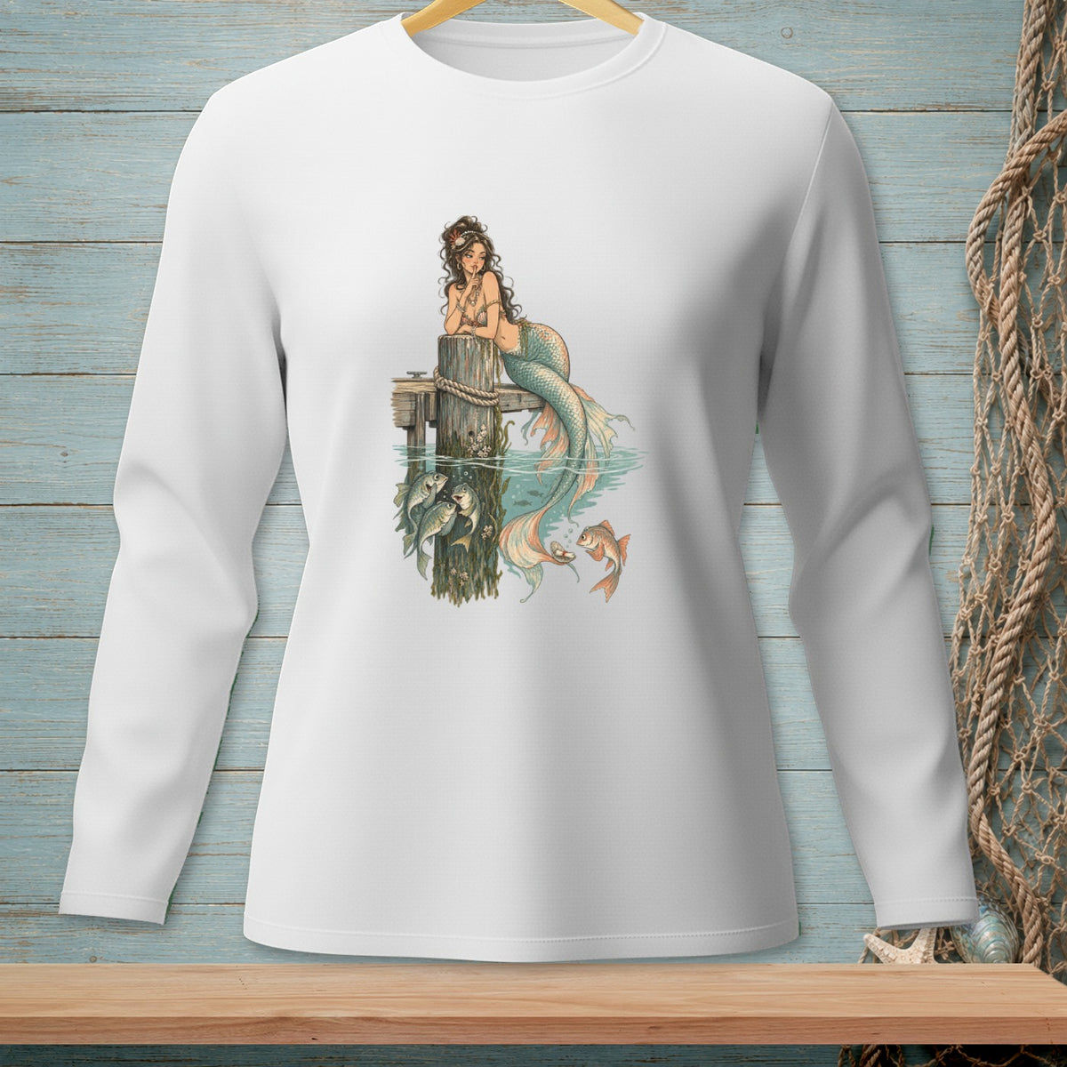White long-sleeve shirt with a graphic of a mermaid sitting on a dock with fish.