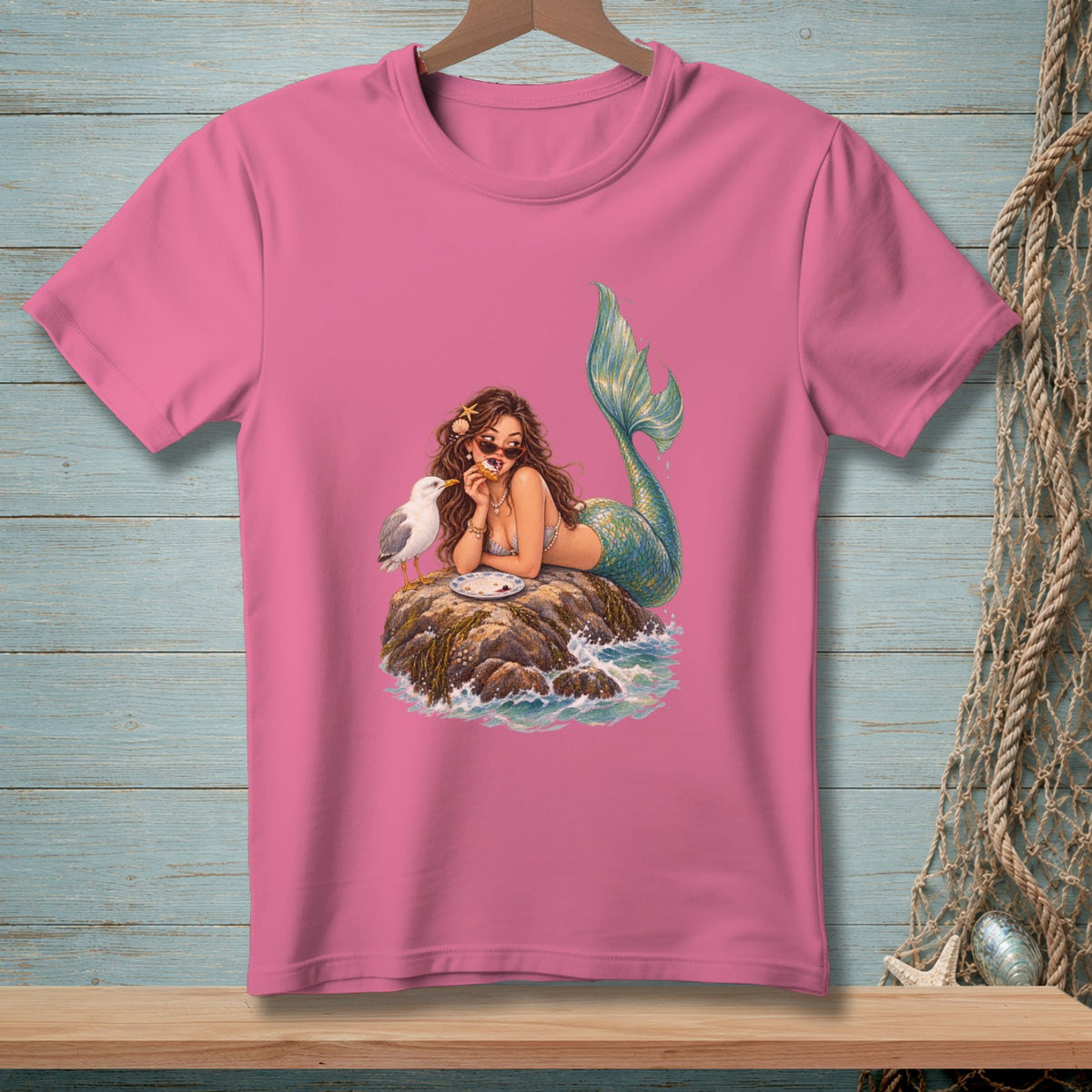 Mermaid with sunglasses shares food with a seagull on a rock in the ocean.