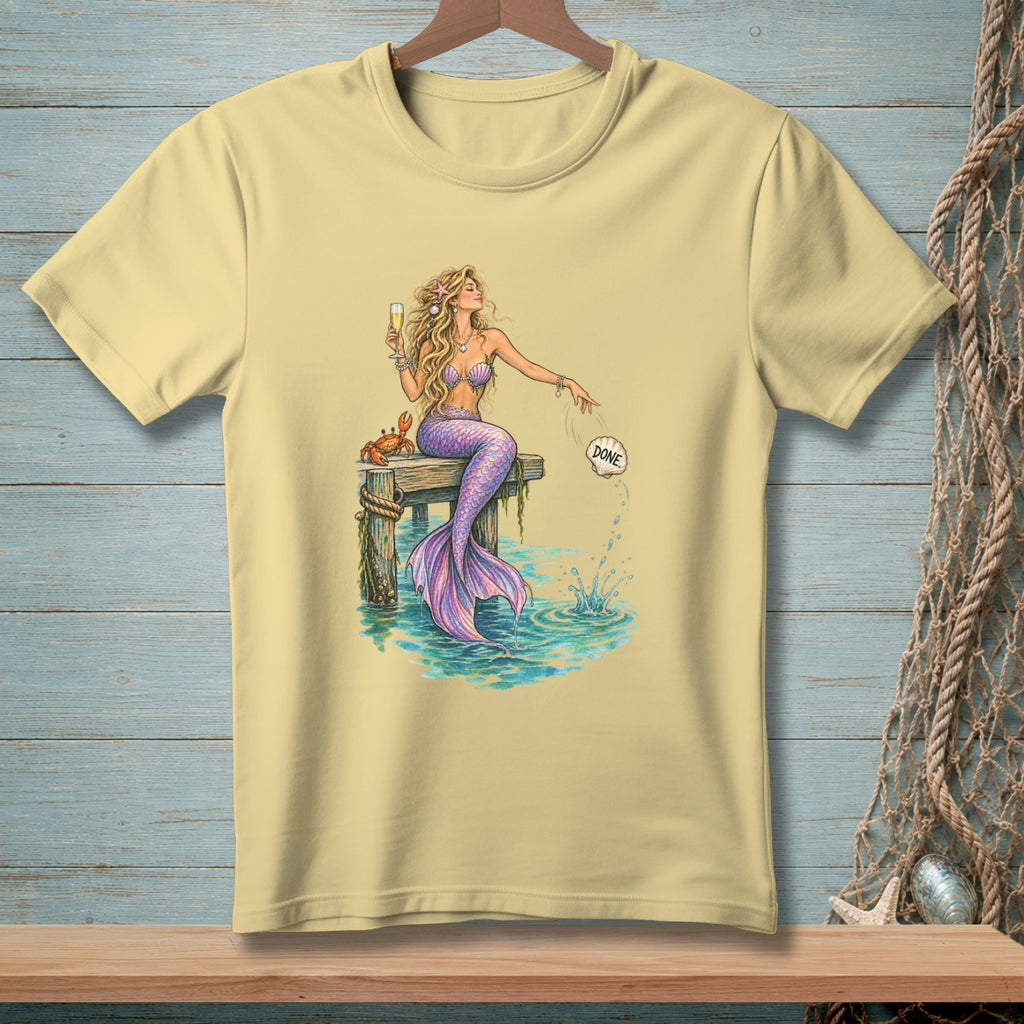 Light yellow t-shirt with a mermaid holding a champagne glass and a crab on a dock.