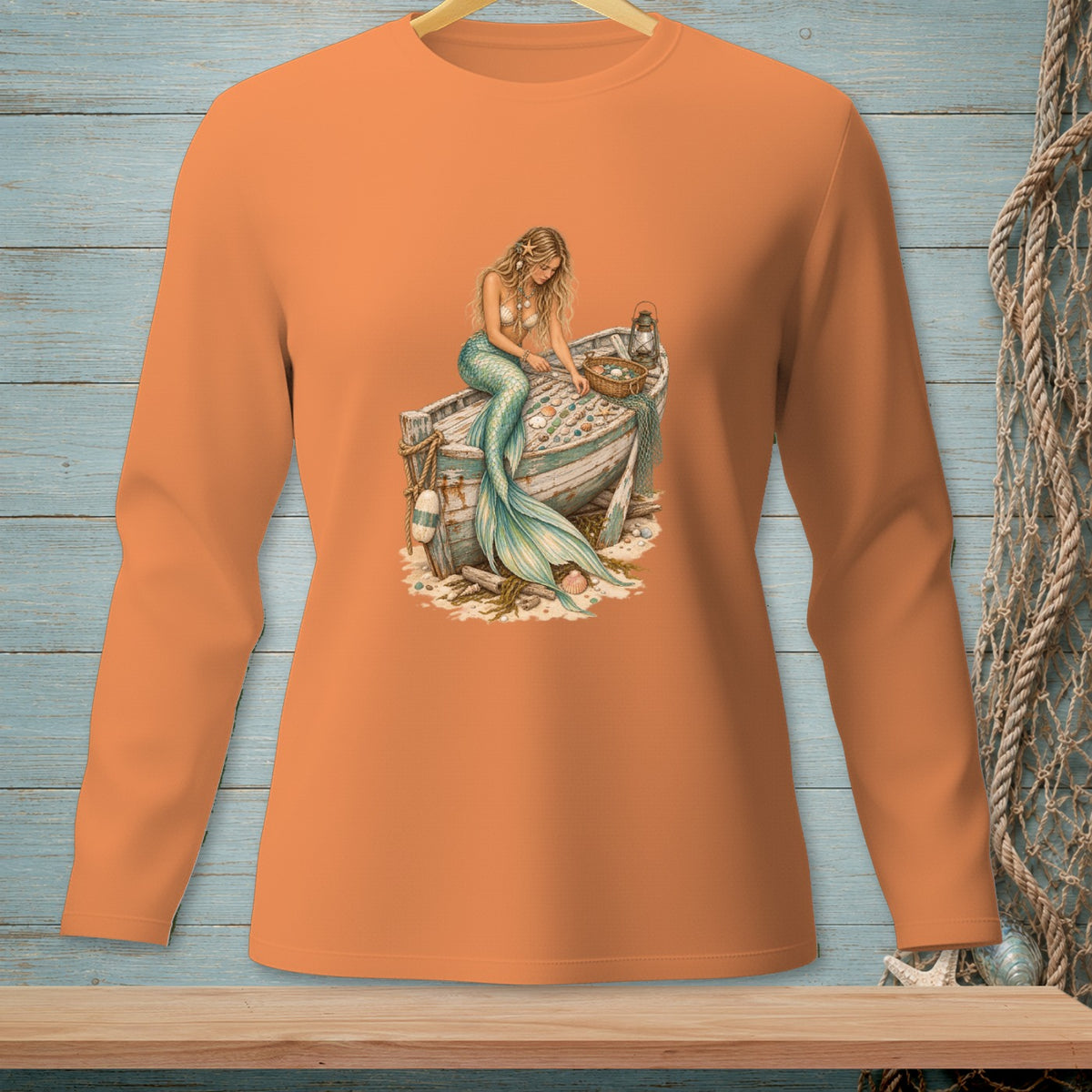Long sleeve orange shirt with a mermaid sitting on a beached rowboat.