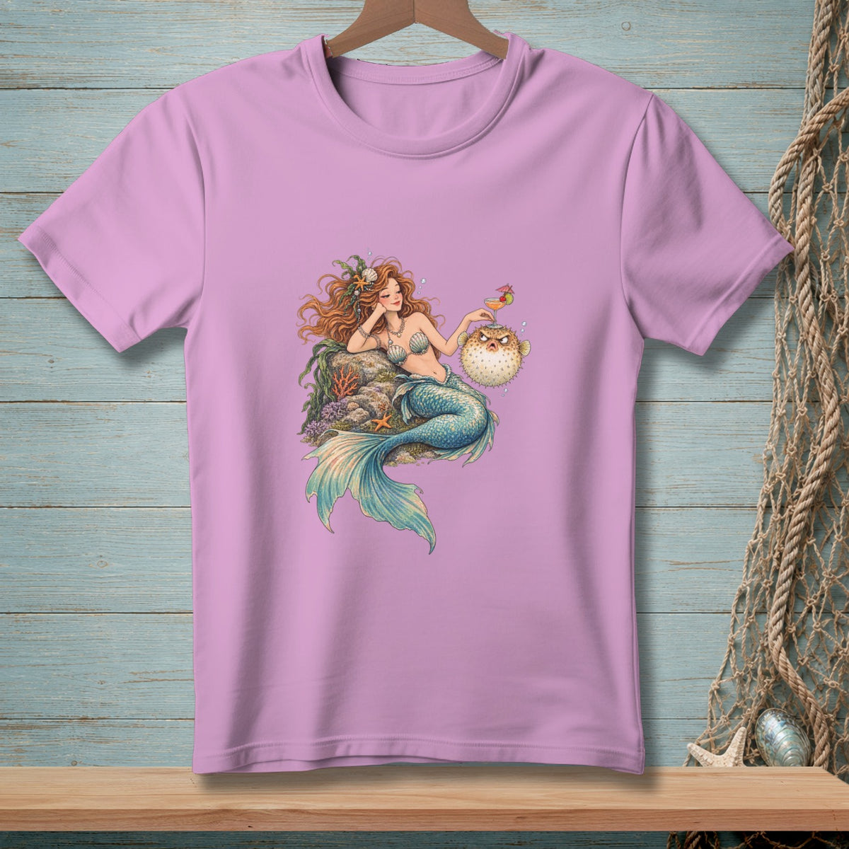 Lavender t-shirt with a cartoon mermaid holding a drink next to a pufferfish.