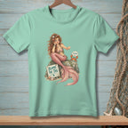 Mermaid with pink tail sitting on rock next to sign "BLAME THE TAIL".