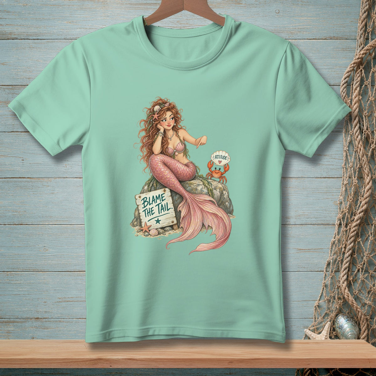 Mermaid with pink tail sitting on rock next to sign "BLAME THE TAIL".