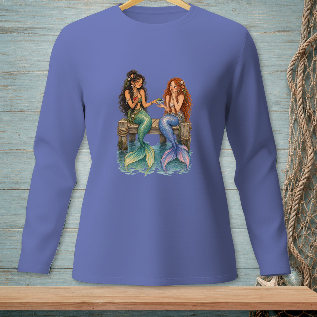 Two mermaids with colorful tails sit on a dock, sharing a bowl of fruit.