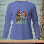 Two mermaids with colorful tails sit on a dock, sharing a bowl of fruit.