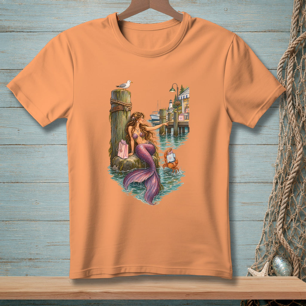 Orange t-shirt with mermaid, crab, seagull, and shops at a dock.