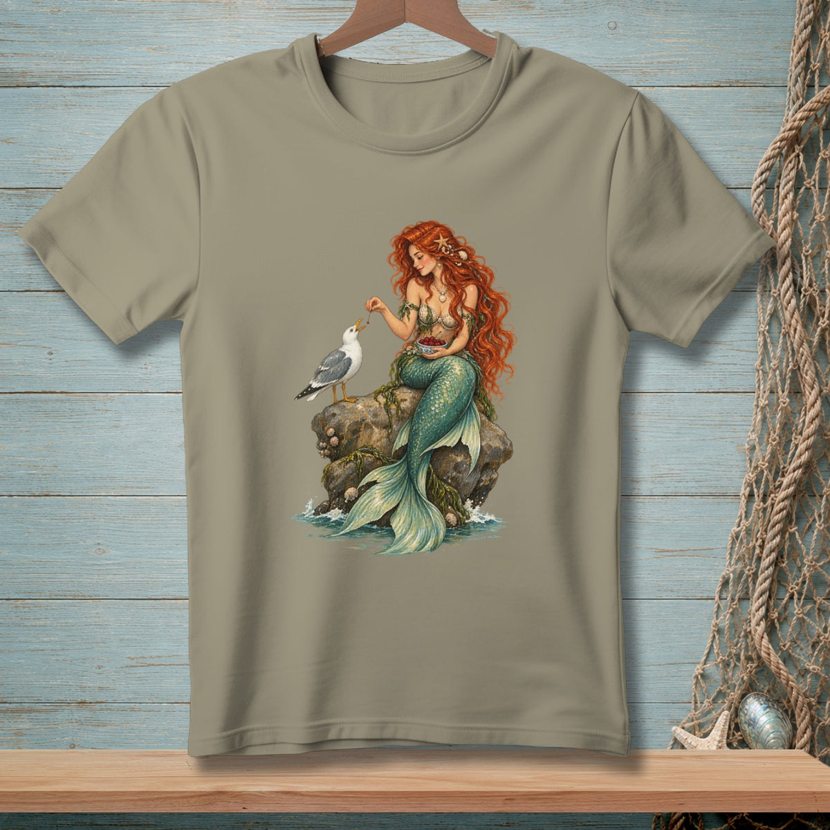 Mermaid with red hair feeding a seagull from a bowl on a rock.