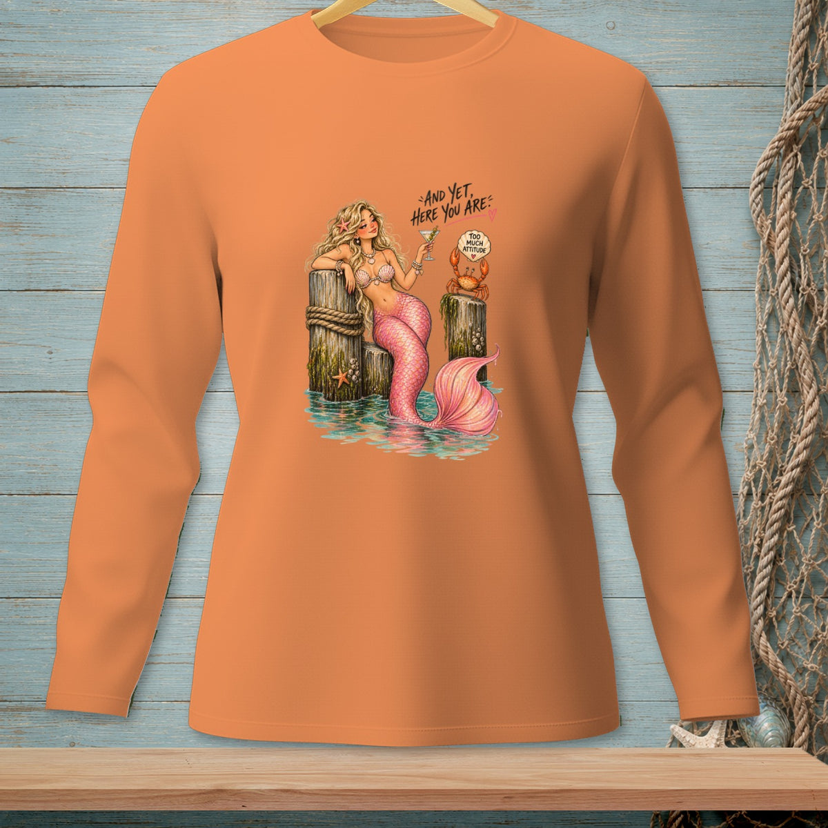 Orange long-sleeve shirt with mermaid, crab, and text "AND YET, HERE YOU ARE: TOO MUCH ATTITUDE".