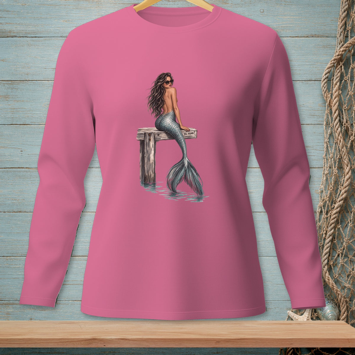Pink long sleeve shirt with mermaid and "YOU AGAIN?" text on wooden dock.