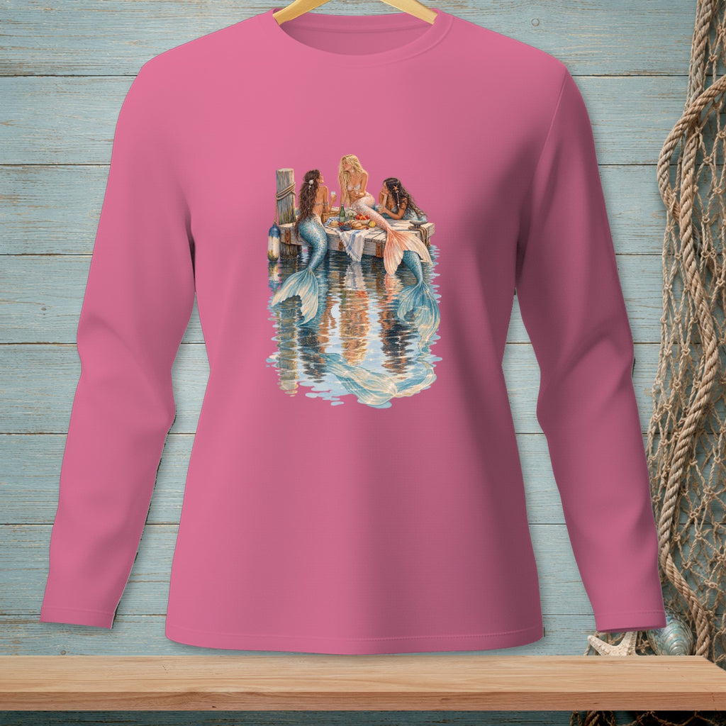 Three mermaids sit on a dock, reflected in the water below.