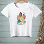White t-shirt with a graphic of three mermaids having a party on a table.