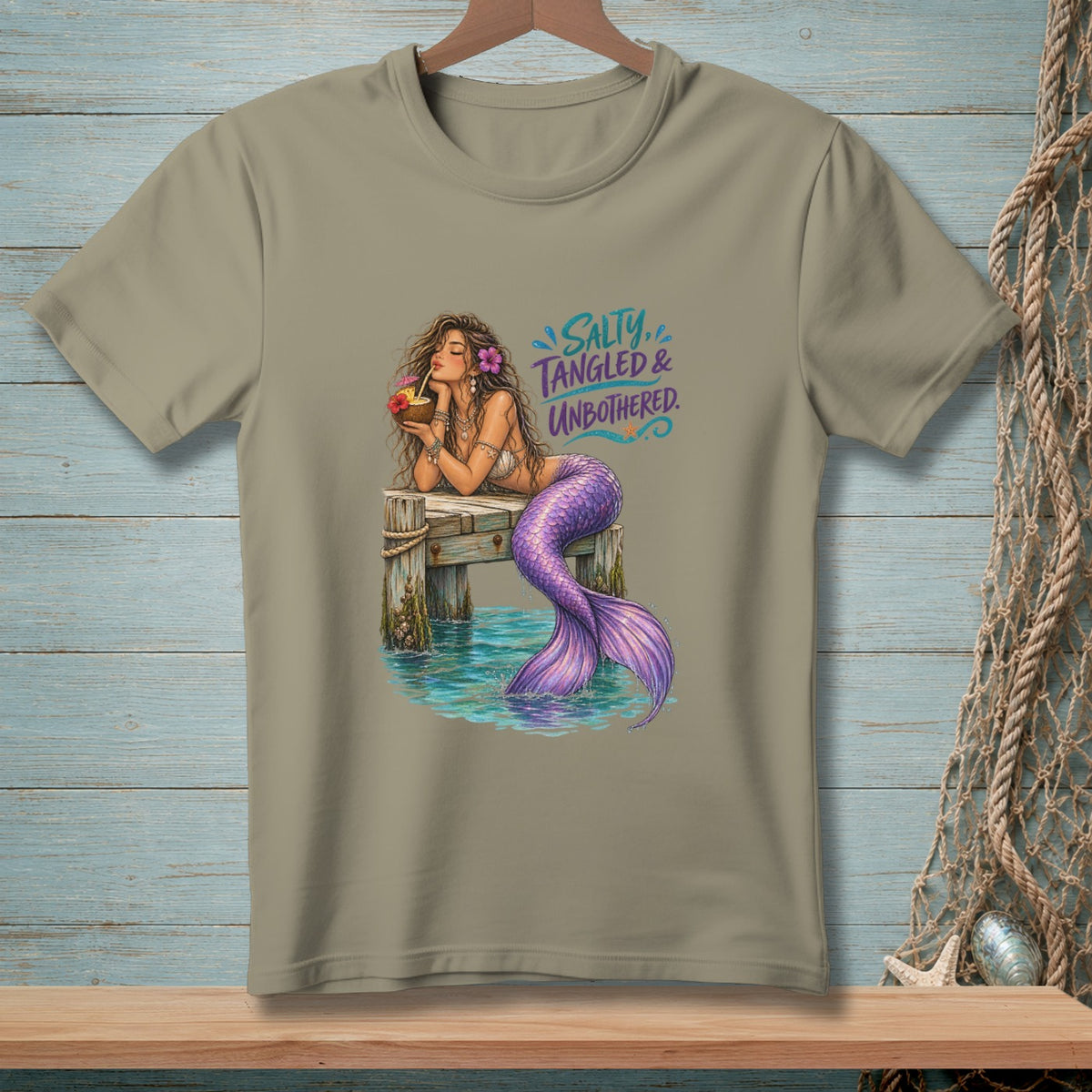 Mermaid with purple tail drinks from coconut on pier, text "Salty, Tangled & Unbothered."