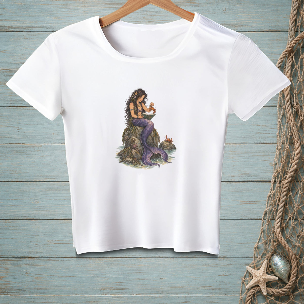 White t-shirt with illustration of a mermaid on rocks holding a crab.