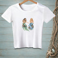 White t-shirt with watercolor illustration of two mermaids sitting on rocks.