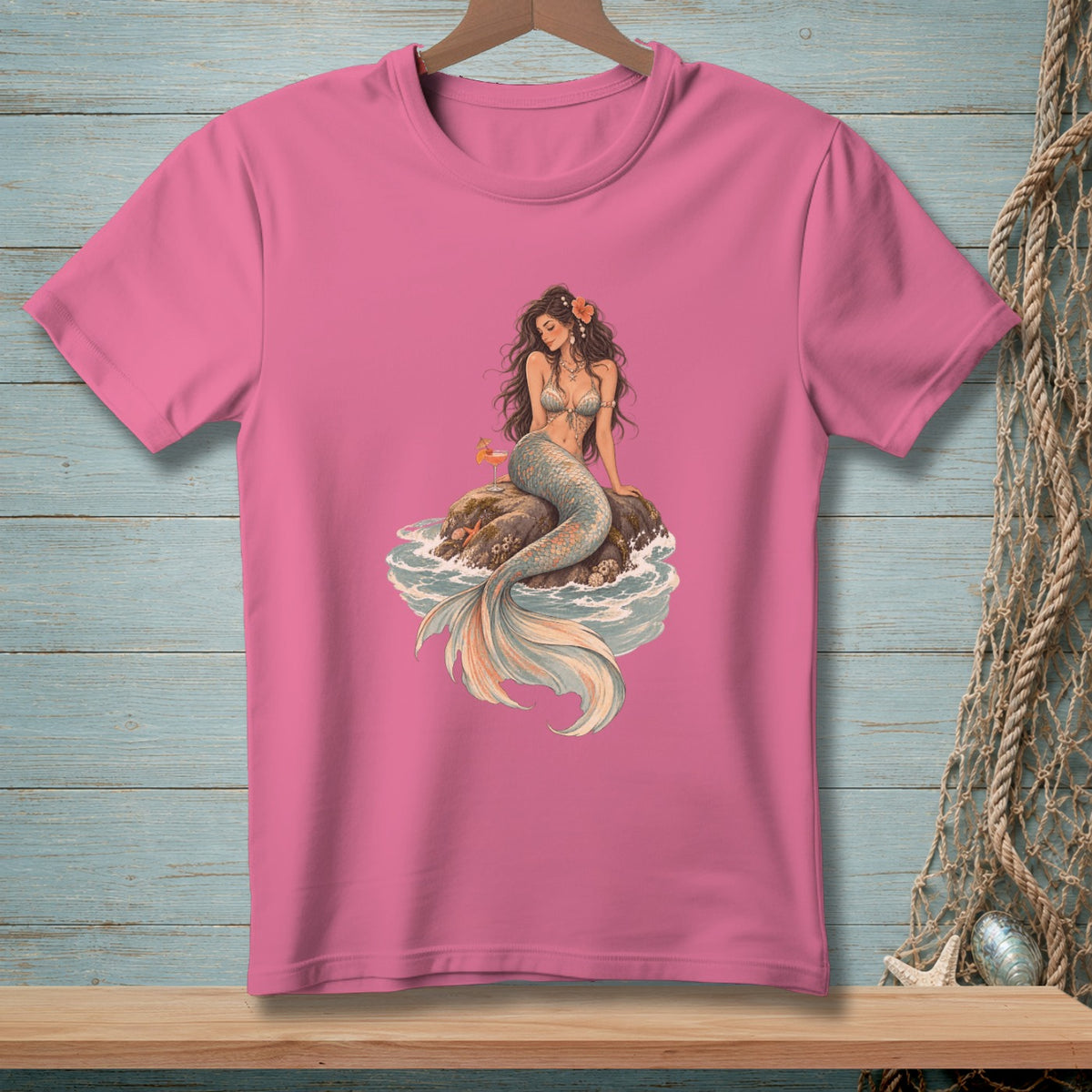Pink t-shirt with a seated mermaid on a rock in waves graphic.