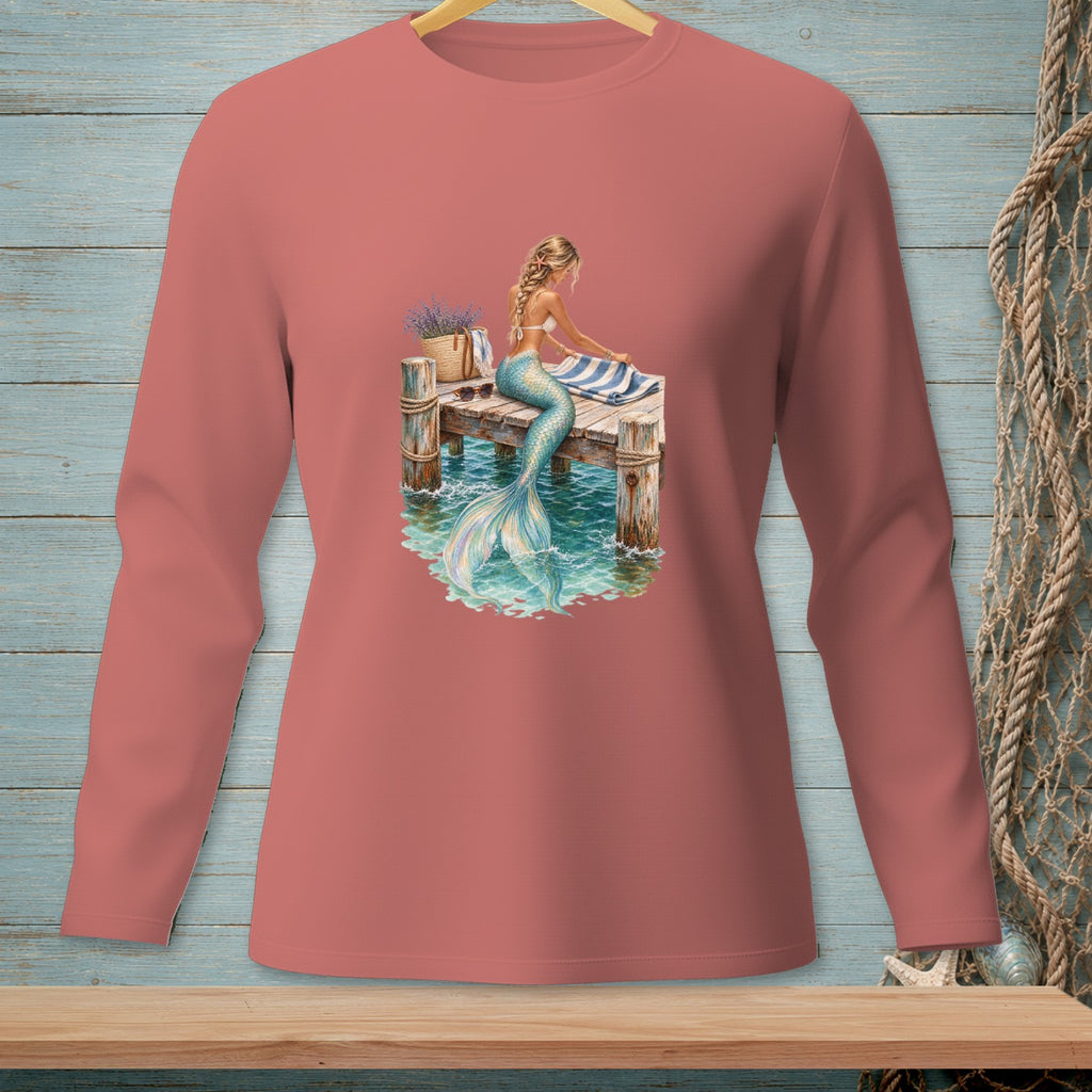 Long-sleeved salmon shirt with mermaid sitting on pier beside striped towel and basket.