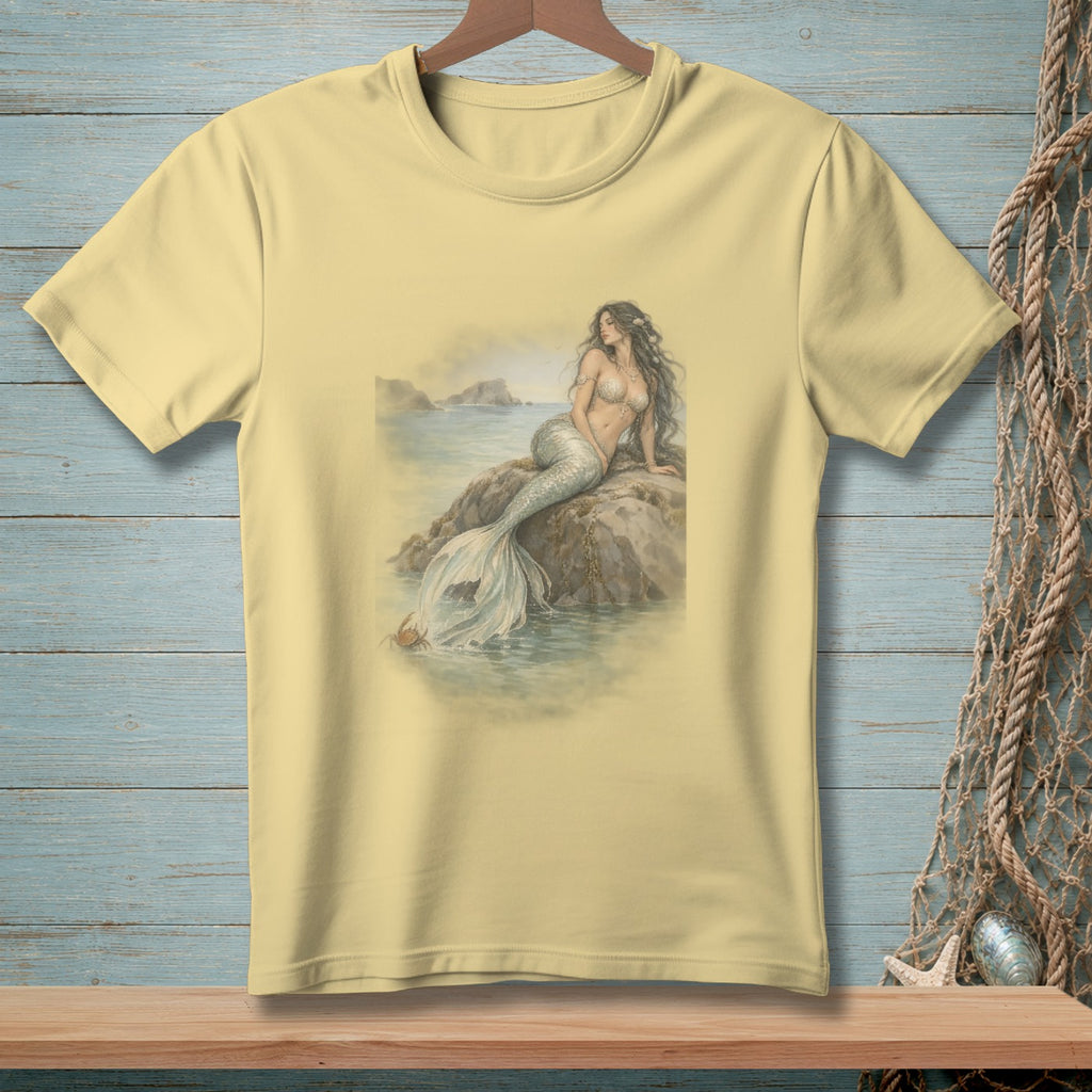 Light yellow t-shirt with a watercolor-style mermaid sitting on a rock by the sea.