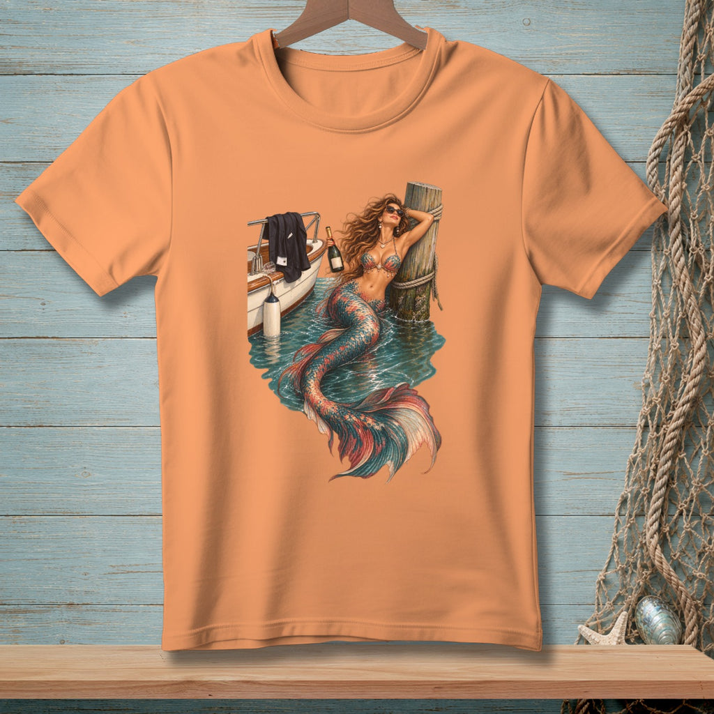 Orange t-shirt with a mermaid leaning on a dock next to a boat.