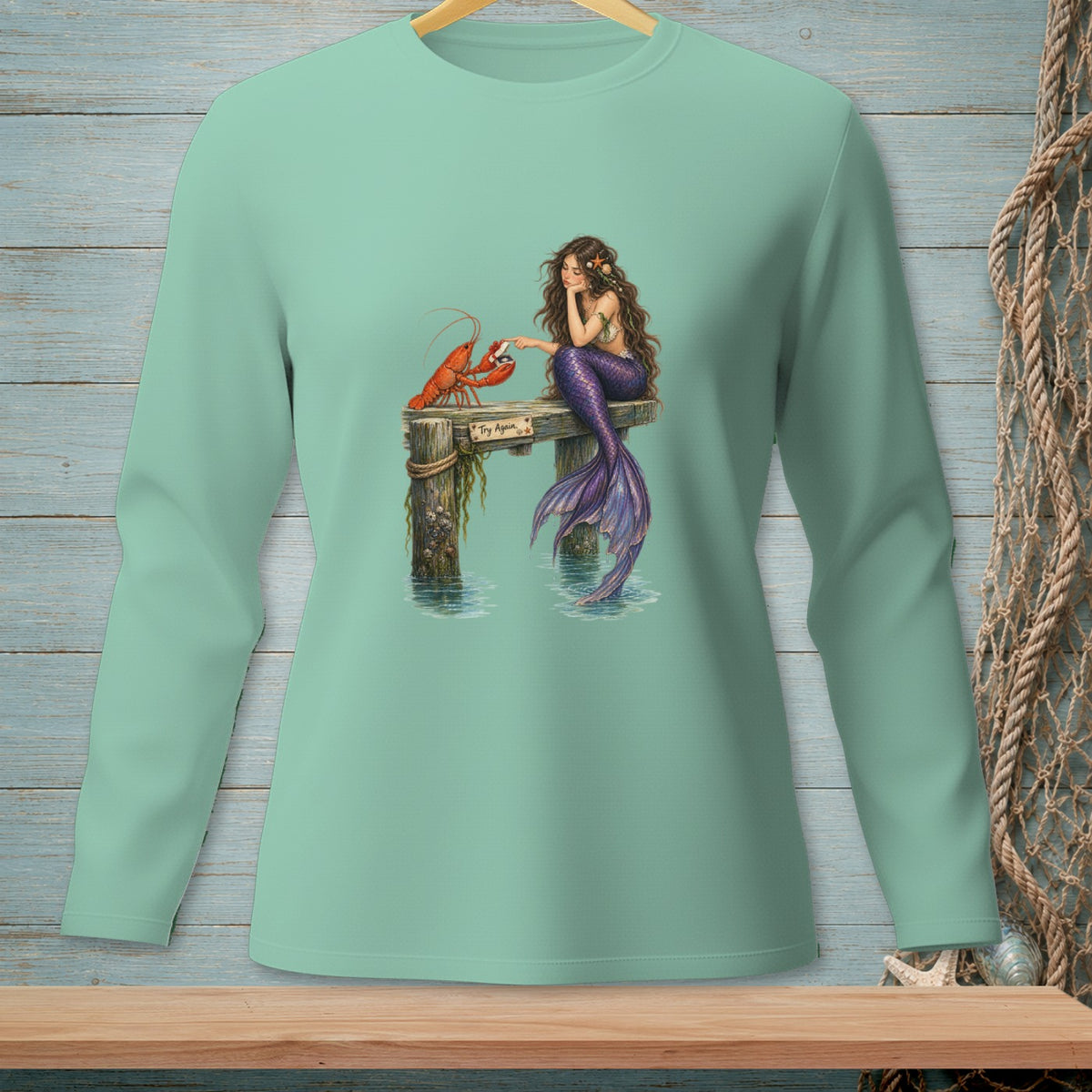 Mermaid and lobster on dock with "Try Again" sign, on mint long-sleeve shirt.