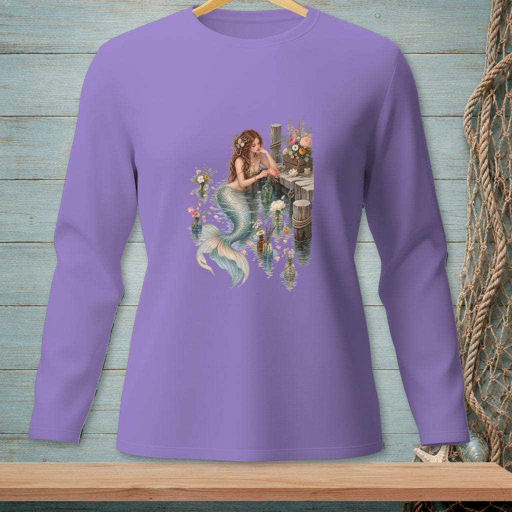 Lavender long sleeve shirt with a mermaid sitting by a wooden dock surrounded by flowers.