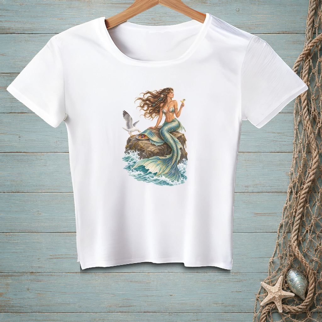 White t-shirt with a mermaid and seagull design on a rock by the sea.