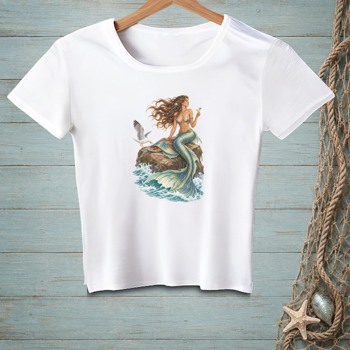 White t-shirt with a mermaid and seagull design on a rock by the sea.