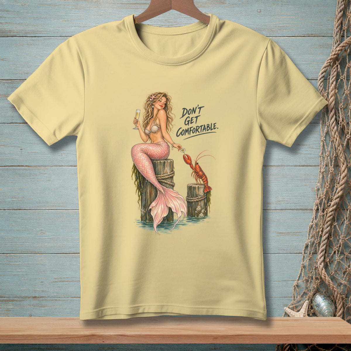 Yellow t-shirt with illustration of a mermaid and lobster with text "Don't Get Comfortable."