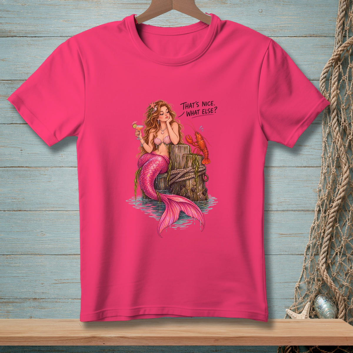 Pink t-shirt with a mermaid, lobster, and cocktail on a post, text reads "That's nice. What else?"