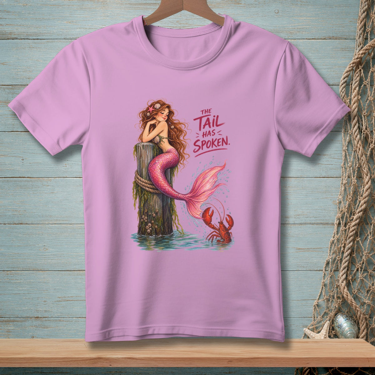 Pink t-shirt with a mermaid sitting on a post, a lobster, and text.