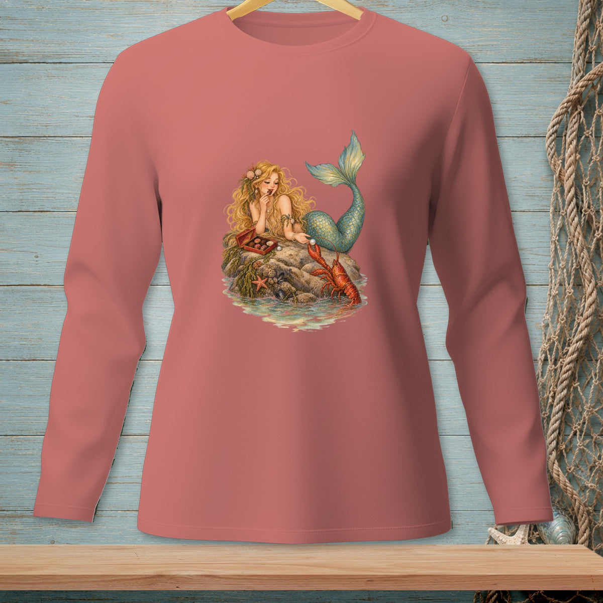 Salmon long-sleeve shirt with mermaid, lobster, and chocolates graphic on a rock.