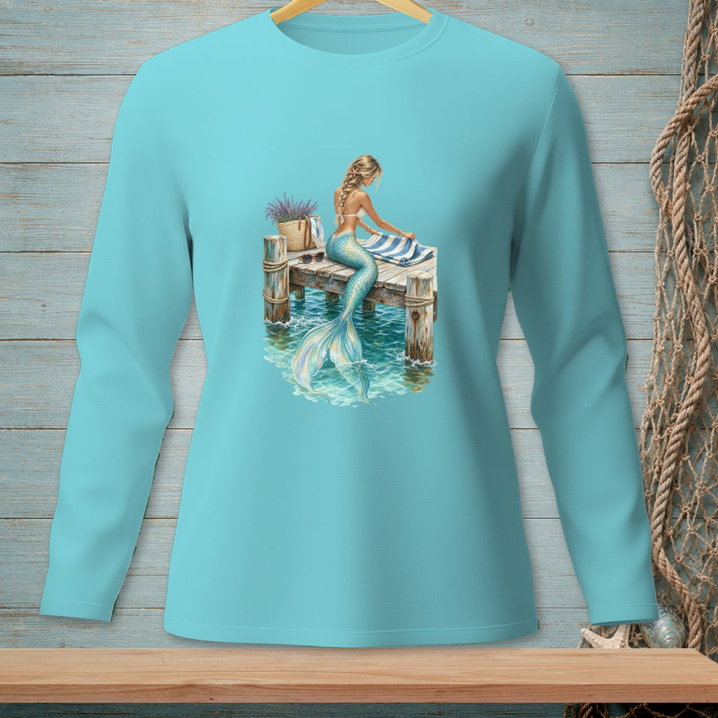 Mermaid sitting on a wooden dock with a striped towel and woven basket.