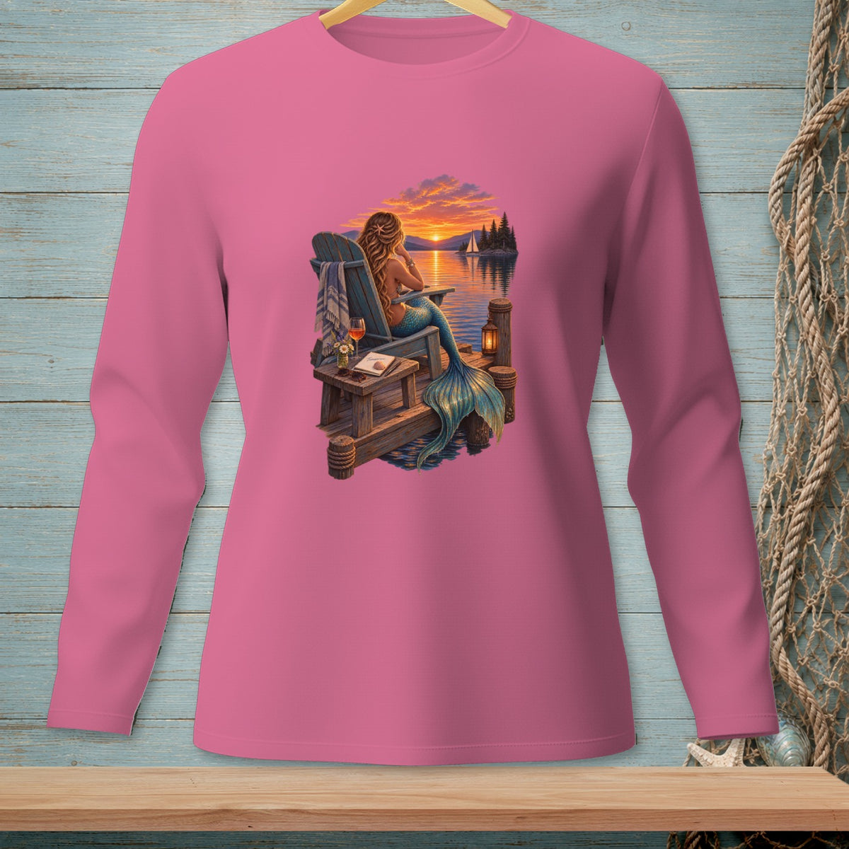 Pink long-sleeve shirt with a graphic of a mermaid sitting by the water at sunset.