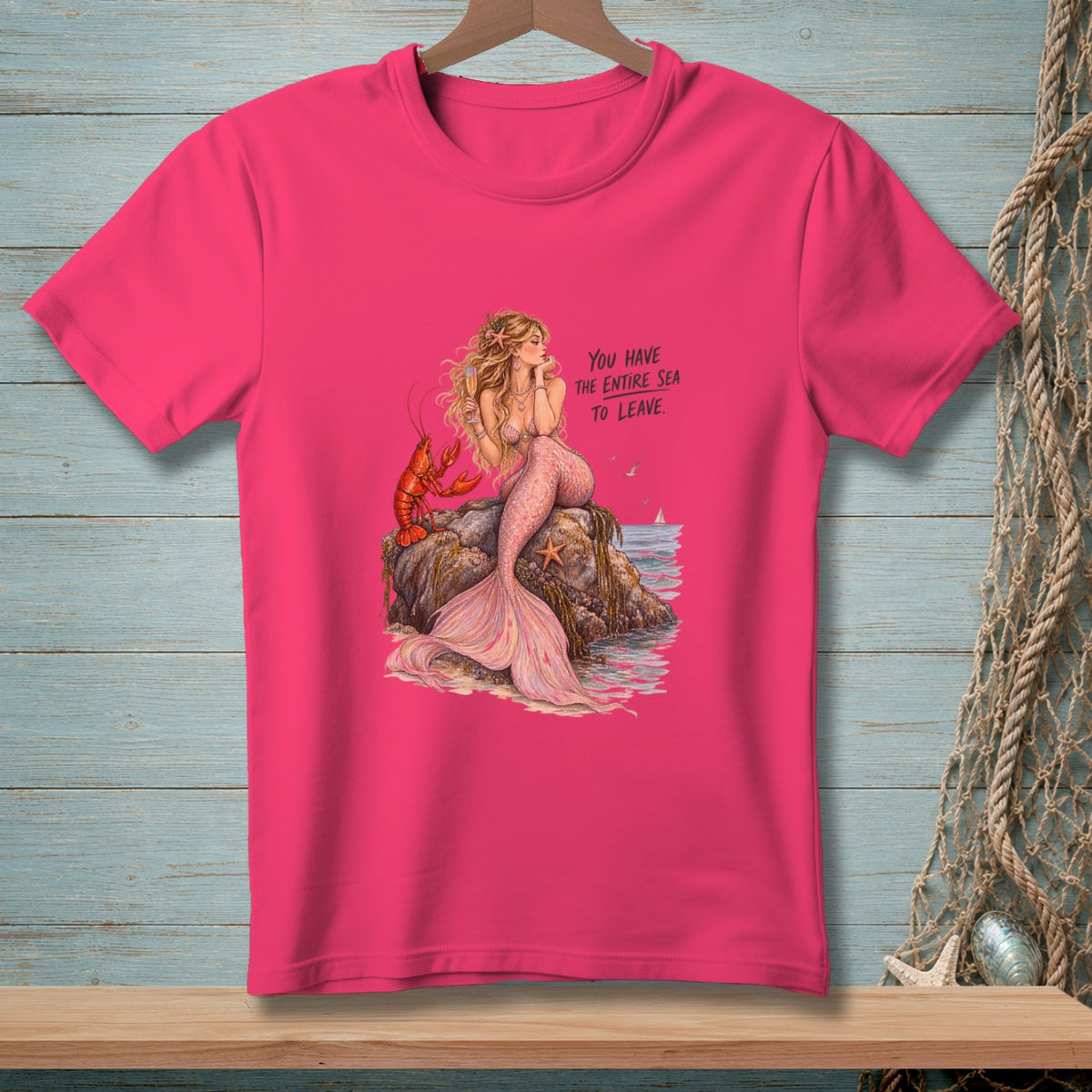 Pink t-shirt with a mermaid, lobster, and text reading "YOU HAVE THE ENTIRE SEA TO LEAVE."