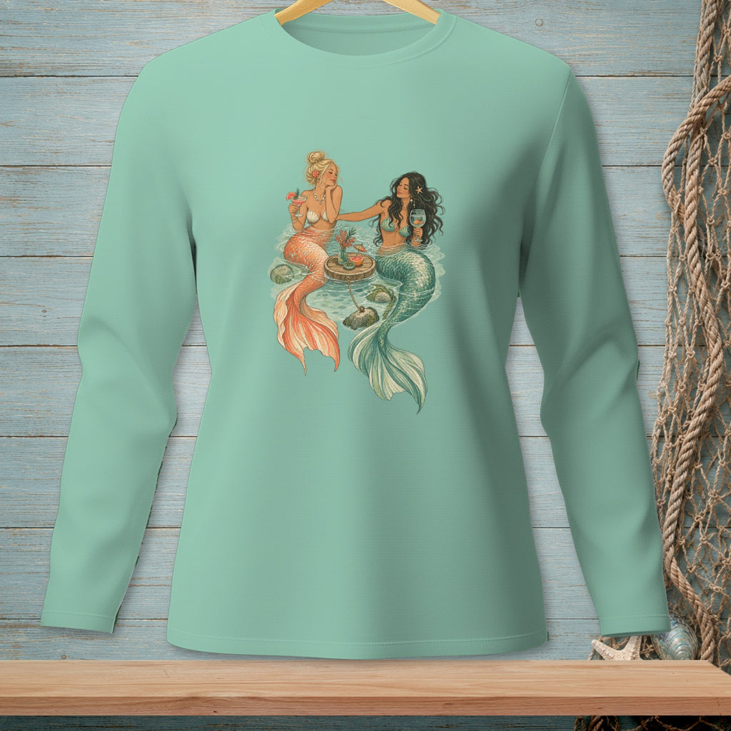 Two mermaids sitting by a small table in the water, one with blonde hair, the other with dark hair.
