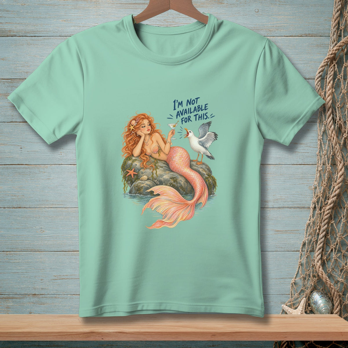 Mint t-shirt with a mermaid and seagull design, reading "I'M NOT AVAILABLE FOR THIS."