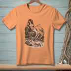 Peach t-shirt with an illustration of a mermaid sitting on rocks by the sea.