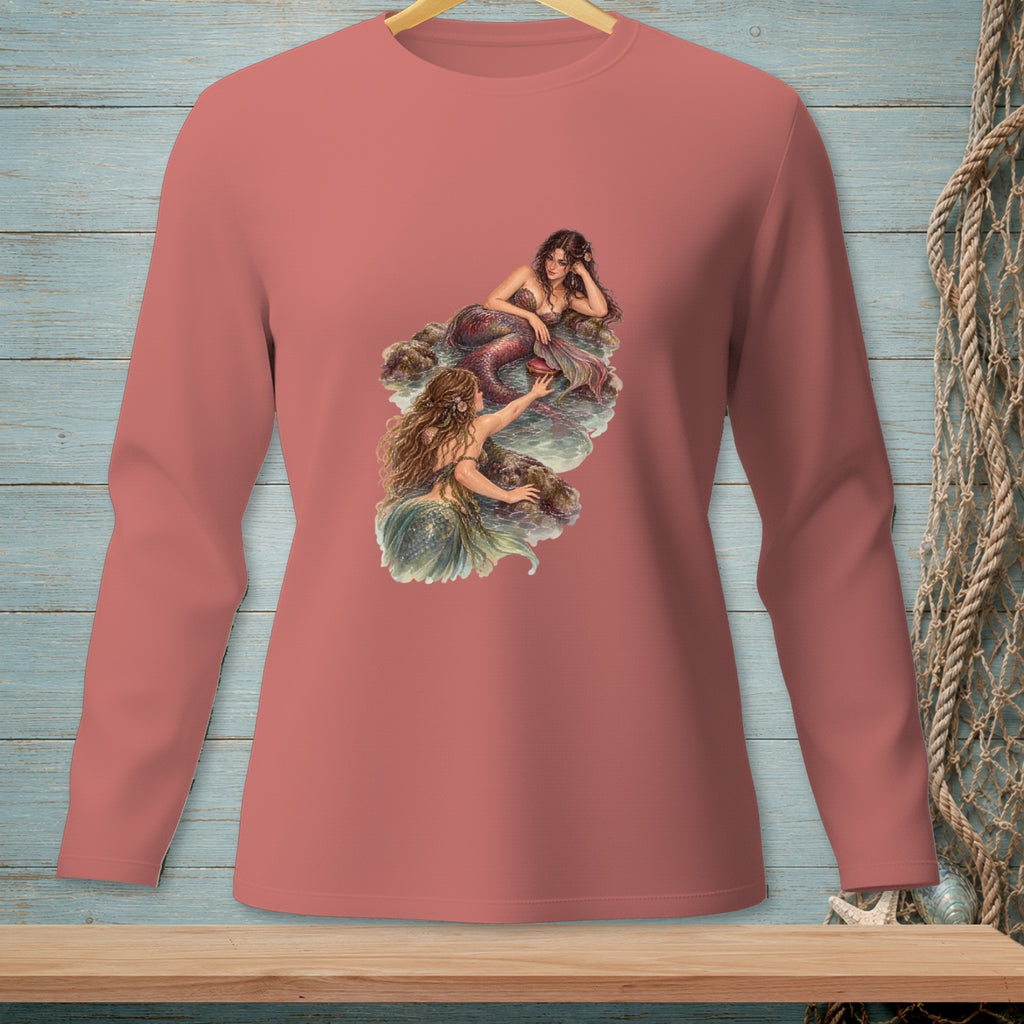 Two mermaids, one with a red tail, on rocks by the water.