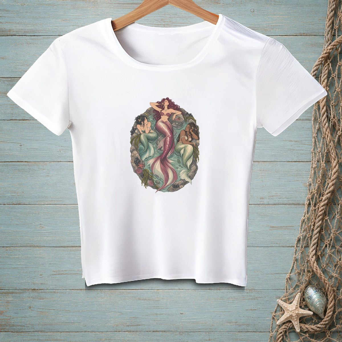 White t-shirt featuring a circular illustration of three mermaids with colorful tails and sea elements.