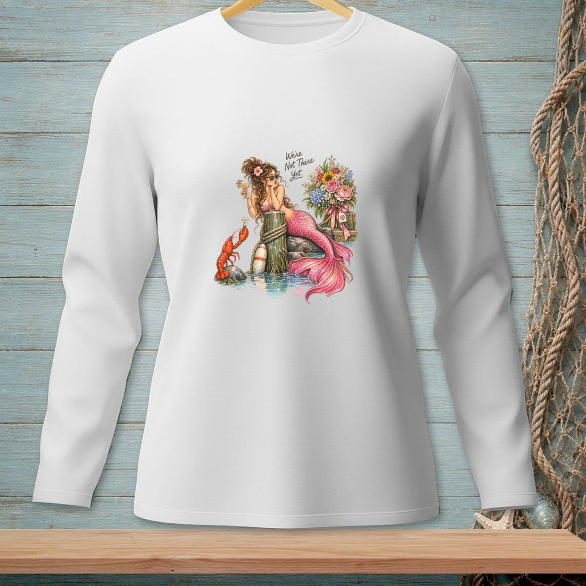 White long-sleeve shirt with mermaid, lobster, flowers, and text "We're Not There Yet."